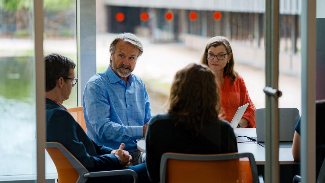 Jim Freeman und drei Kollegen und Kolleginnen sitzen in einem Besprechungsraum.