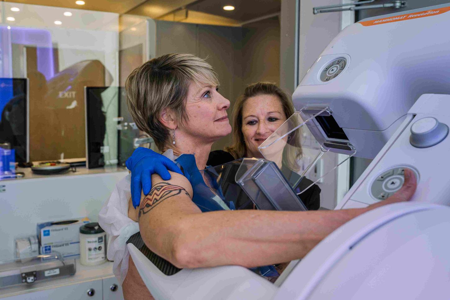 A tech is positioning the patient for her mammogram. Sideview