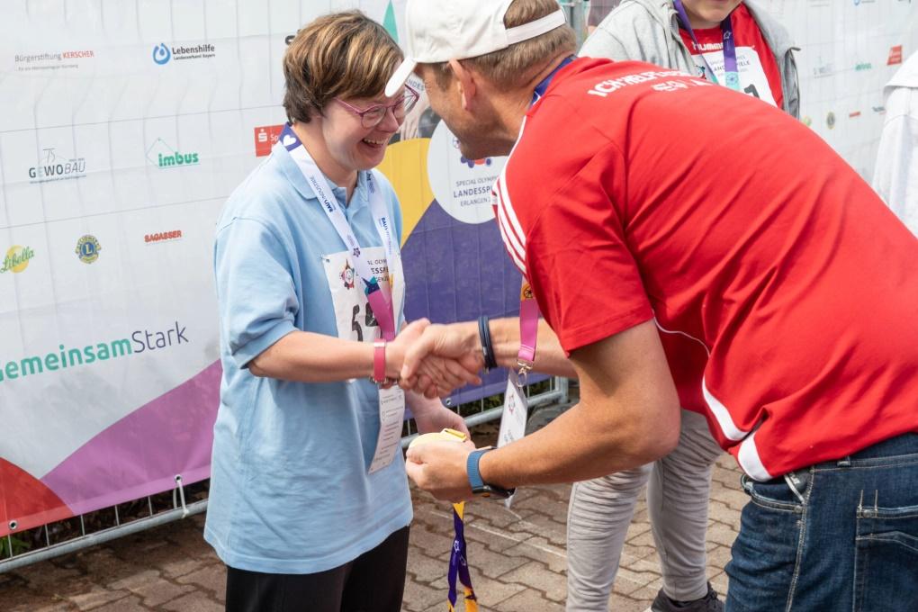 Ein Freiwilliger gibt einer Teilnehmerin der Special Olympics Bayern die Hand.
