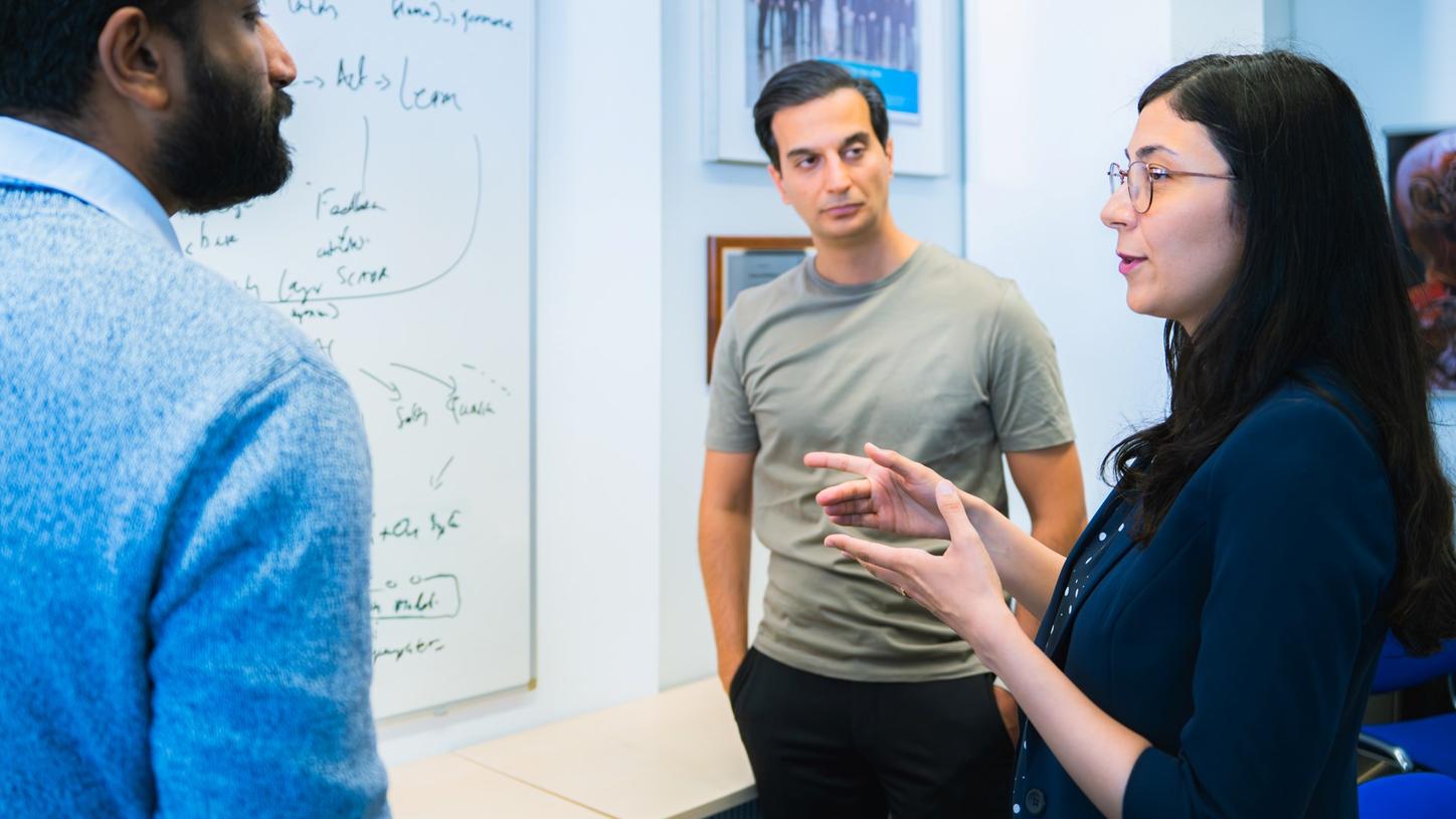 Ullaskrishnan Poikavila discusses ideas with two colleagues in front of a whiteboard in an office setting.