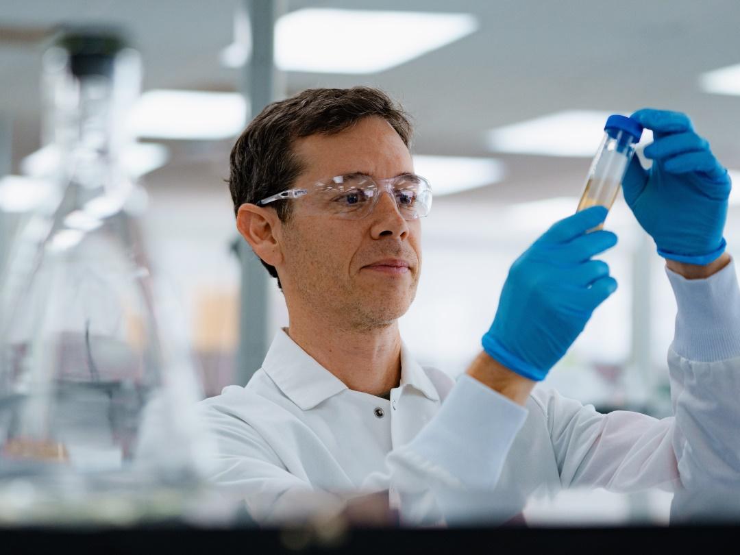 Assay-Entwickler im Labor, der eine Küvette mit einer Flüssigkeit in der Hand hält.