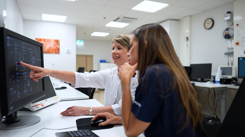 Two radiologists are evaluating MRI scans on a computer screen.