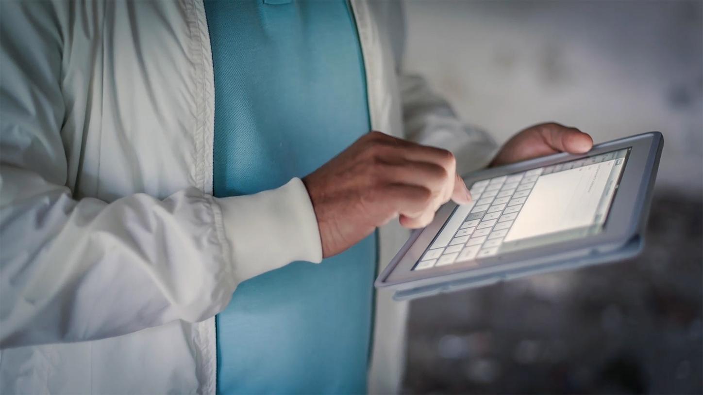 Person tapping on a tablet screen wearing a light jacket and blue shirt