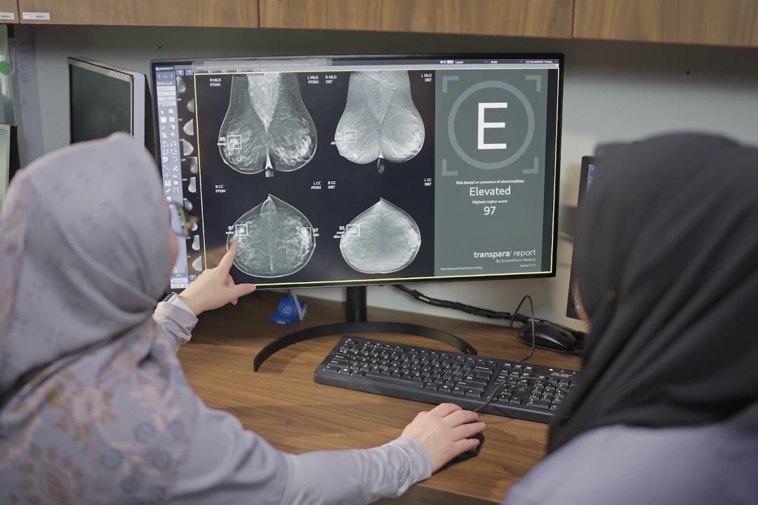 Two women are looking at a breast screening image on a computer screen.