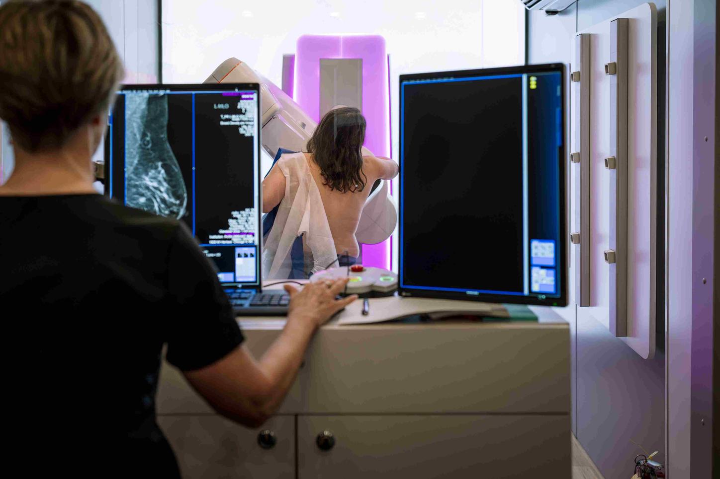 A tech is positioning the patient for her mammogram. View from behind
