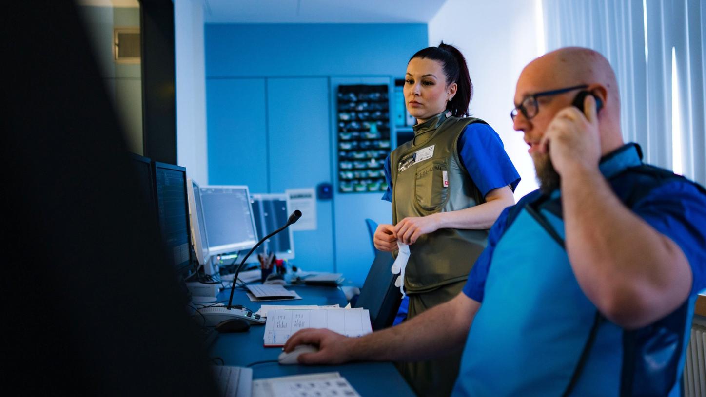 Medizinisches Fachpersonal überwacht in einem Kontrollraum mehrere Bildschirme und steht während eines interventionellen Eingriffs in kontinuierlicher Kommunikation.