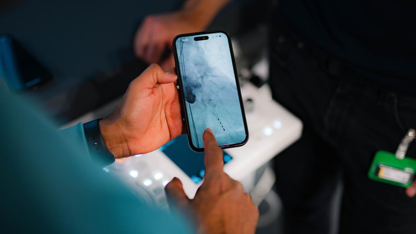 Eine Person hält ein Smartphone, auf dessen Display ein medizinisches Bild zu sehen ist, und zeigt mit dem Finger auf eine Markierung.