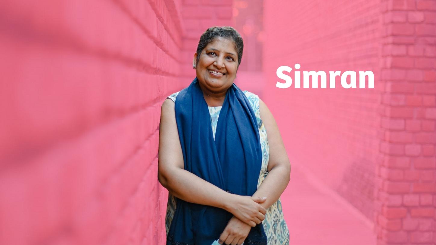 Breast cancer survivor Simran in front of a pink background.