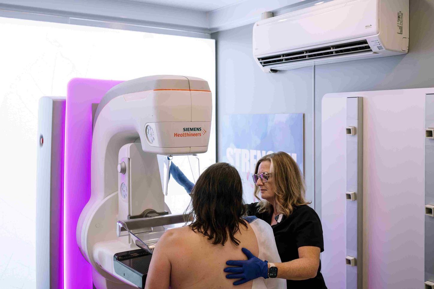 A tech is positioning the patient for her mammogram. View from behind