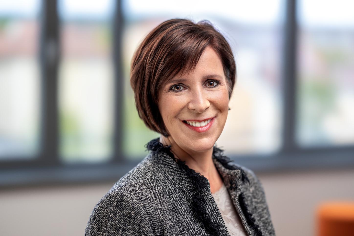 Darleen Caron Darleen Caron with short hair wearing a textured jacket, photographed against a softly blurred office background.