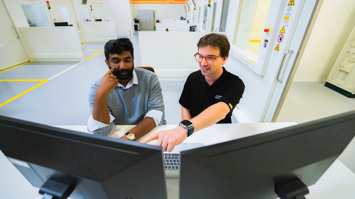 Ullaskrishnan Poikavila and a colleague work together at a computer workstation in a manufacturing environment. The colleague points to information on one of the computer monitors