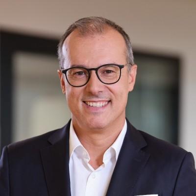 Professional portrait of João Seabra, Head of Americas, wearing glasses and a dark blazer with a white shirt, photographed against a blurred office background.