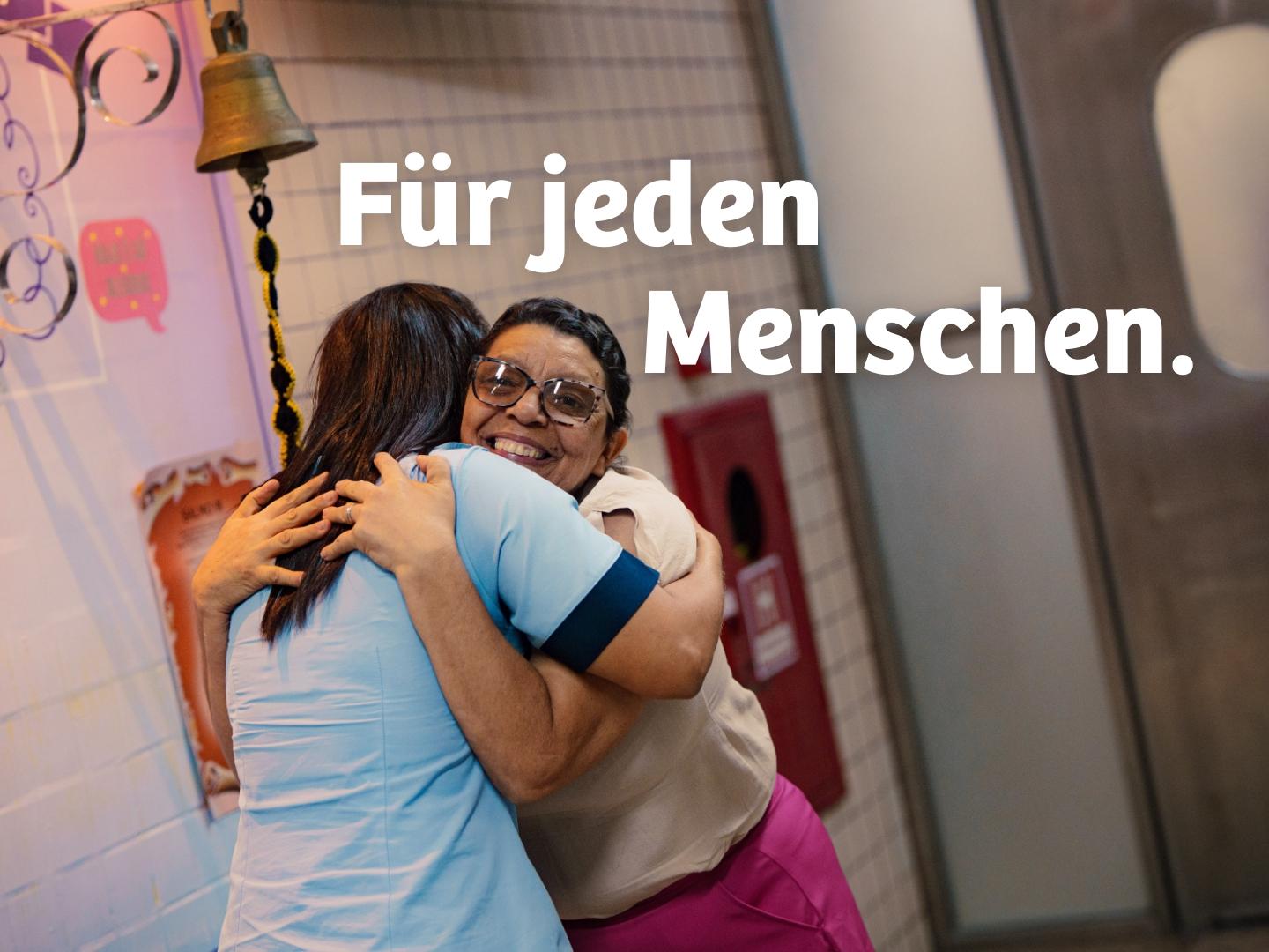 Healthcare worker embracing a smiling woman.
