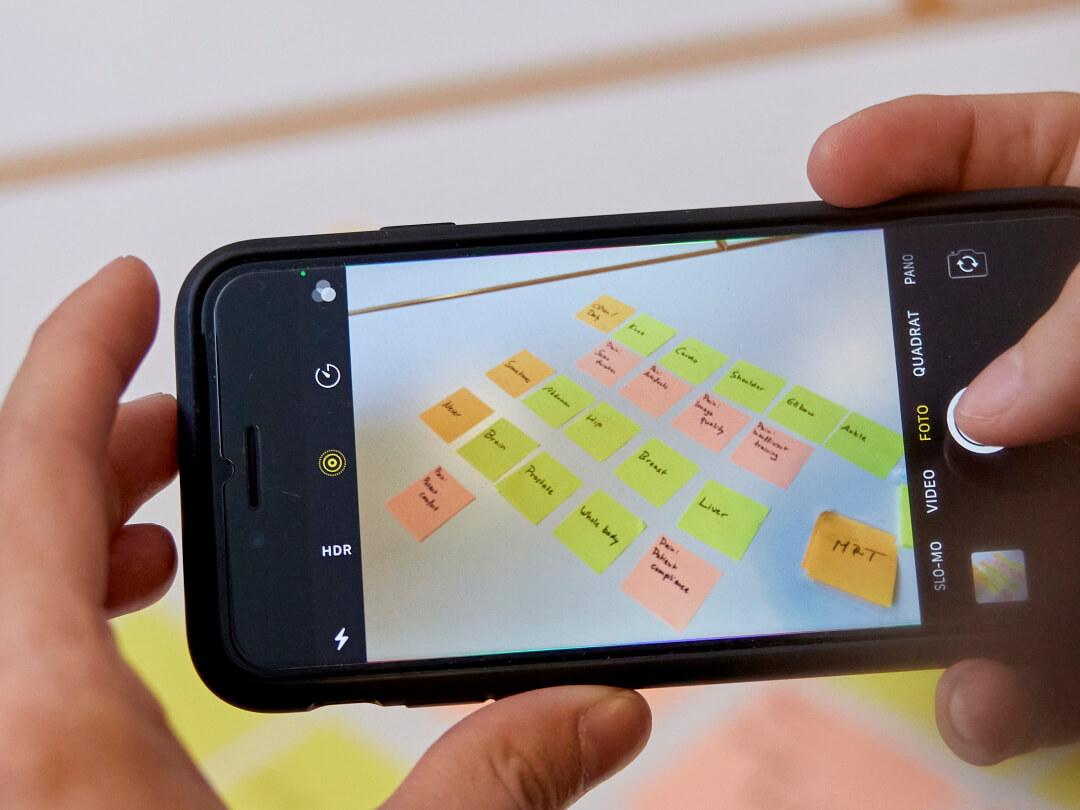 Ein Handy, das die Kamerafunktion zeigt und ein Bild von Klebezetteln auf weißem Hintergrund aufnimmt.